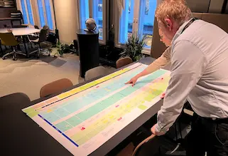 En person peker på et stort utskrevet tjenestekart på et bord